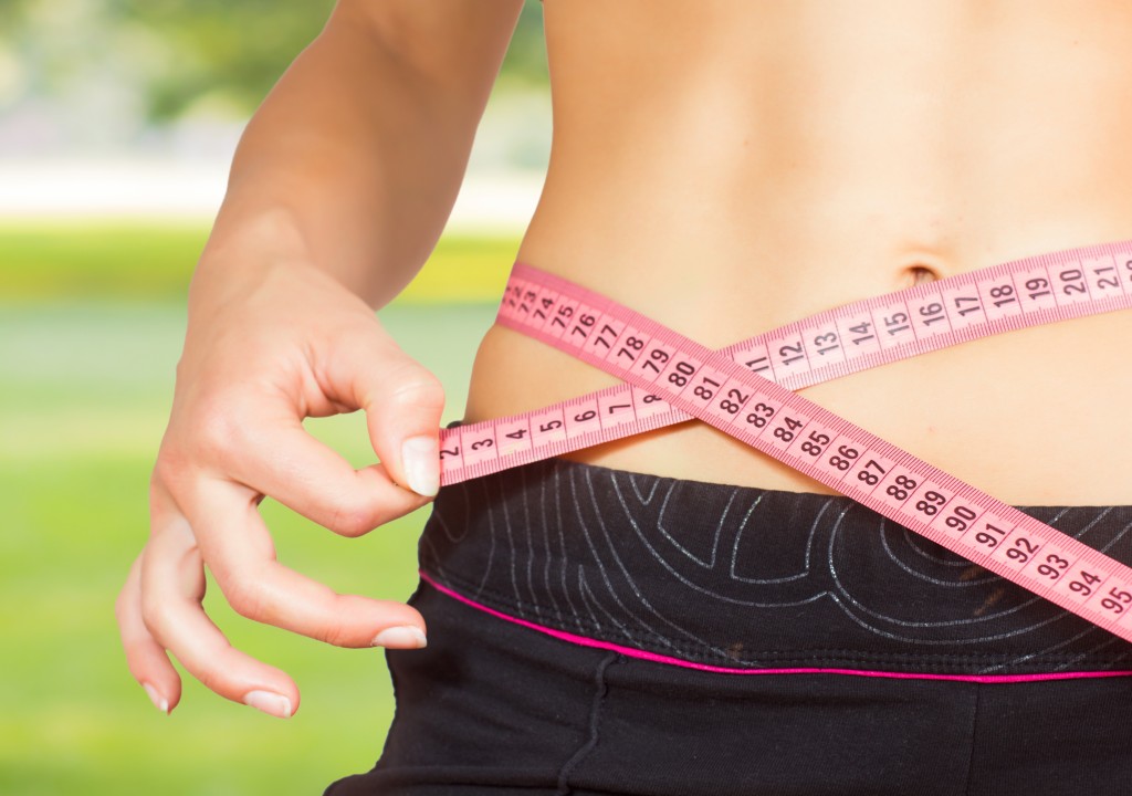 a slim female measuring her waistline with a tape measure