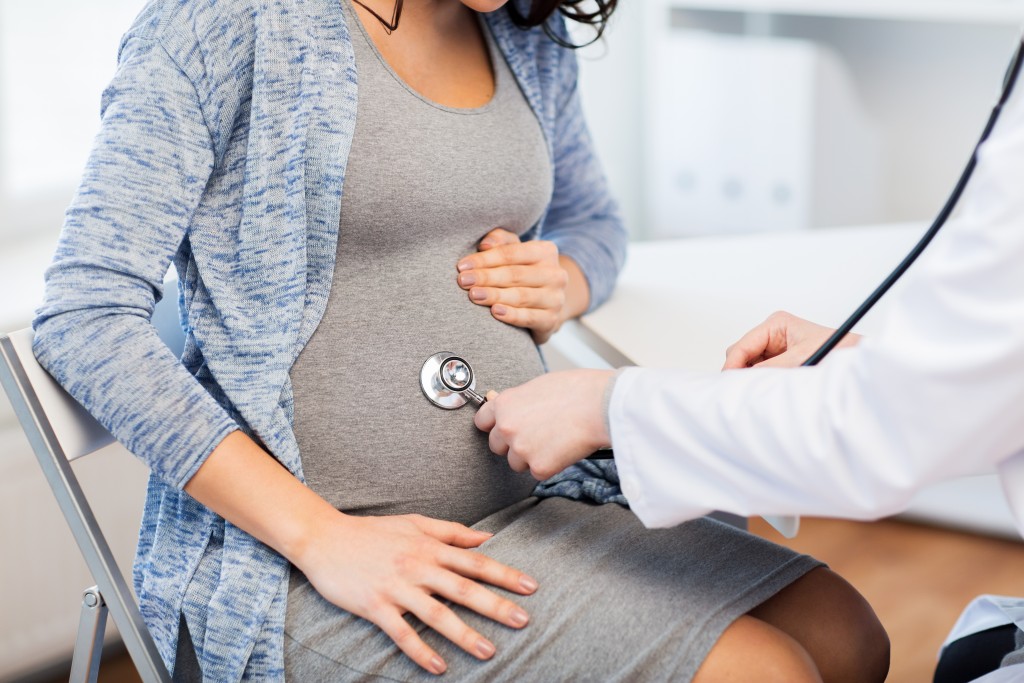 doctor is using the stethoscope on a pregnant woman's stomach