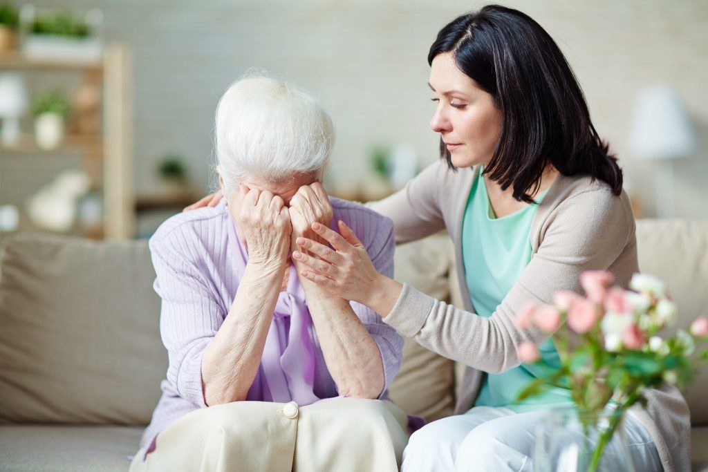 elderly woman is crying while being comforted by her carer