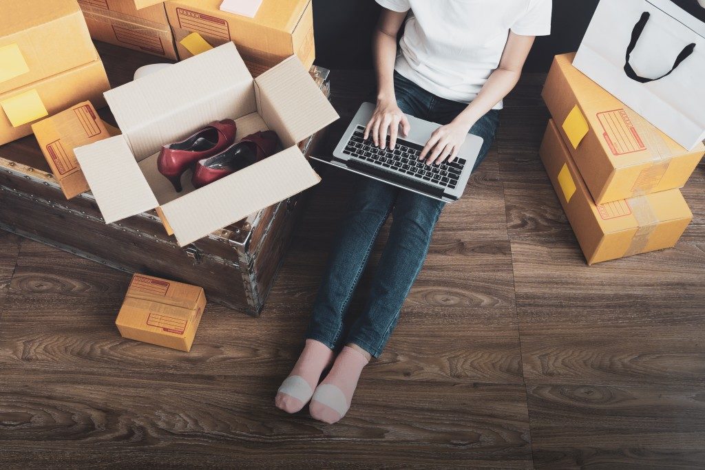 Woman using laptop while sitting on floor beside boxes