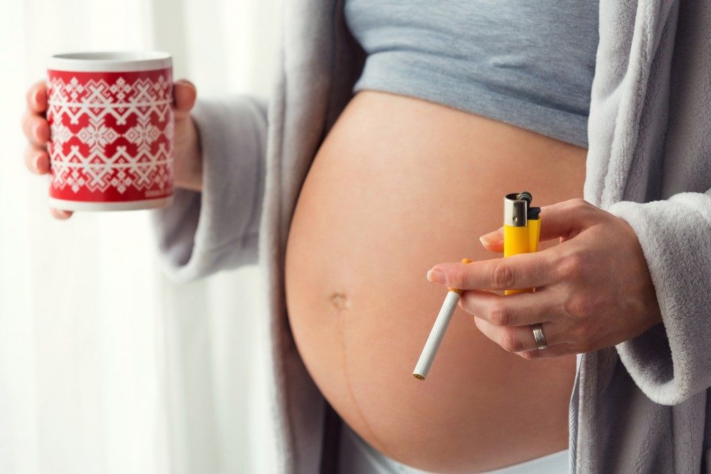 Pregnant woman smoking a cigarette and holding a mug