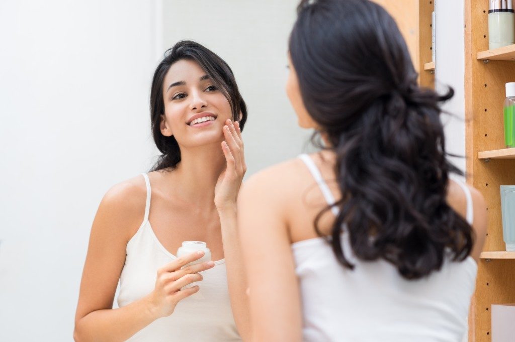 Young woman applying moisturizer on her face