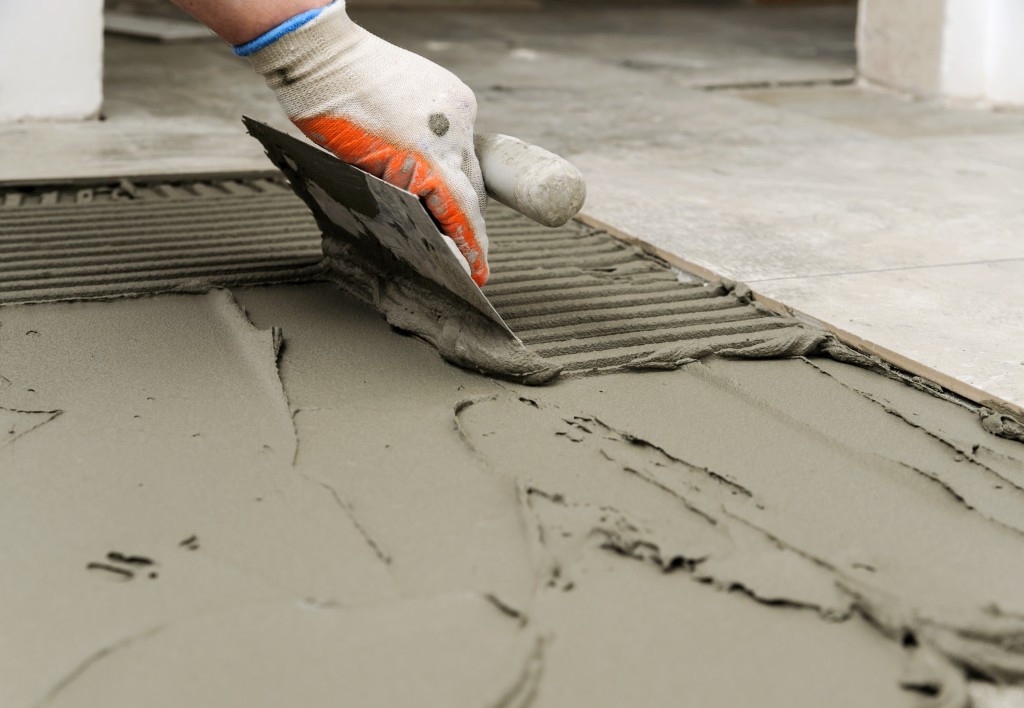 Troweling mortar onto a concrete floor in preparation for laying floor tile