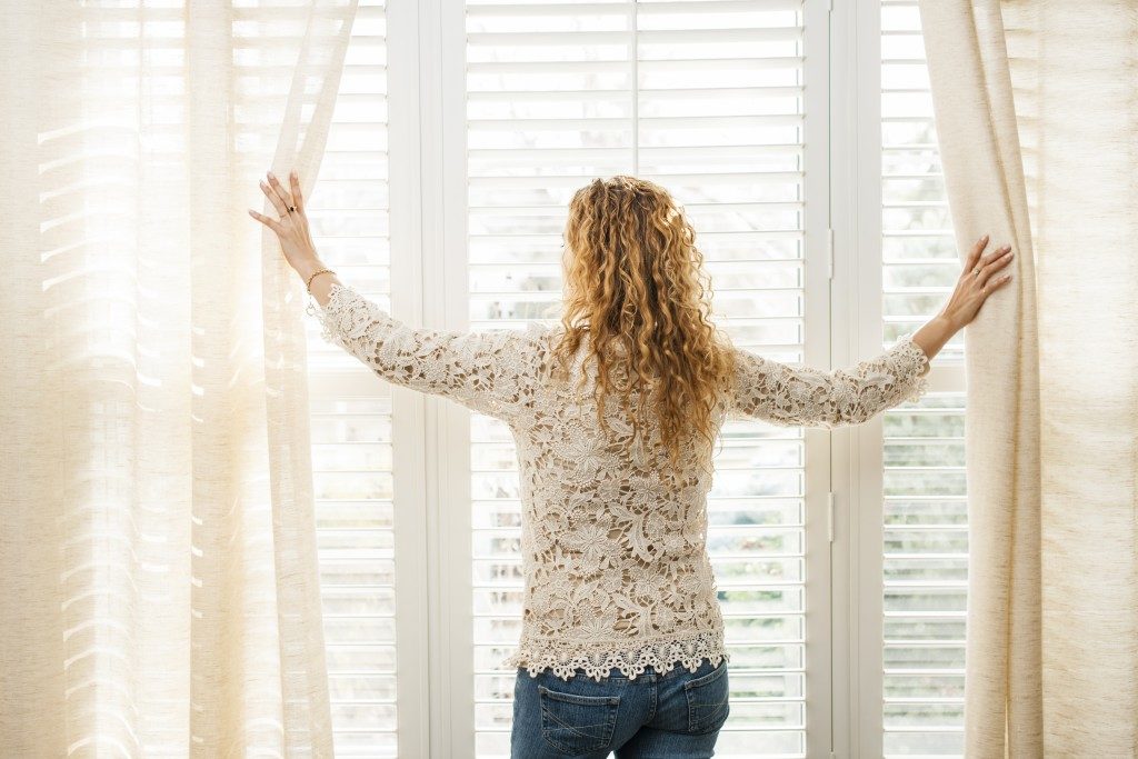 woman parting the curtains of a large window