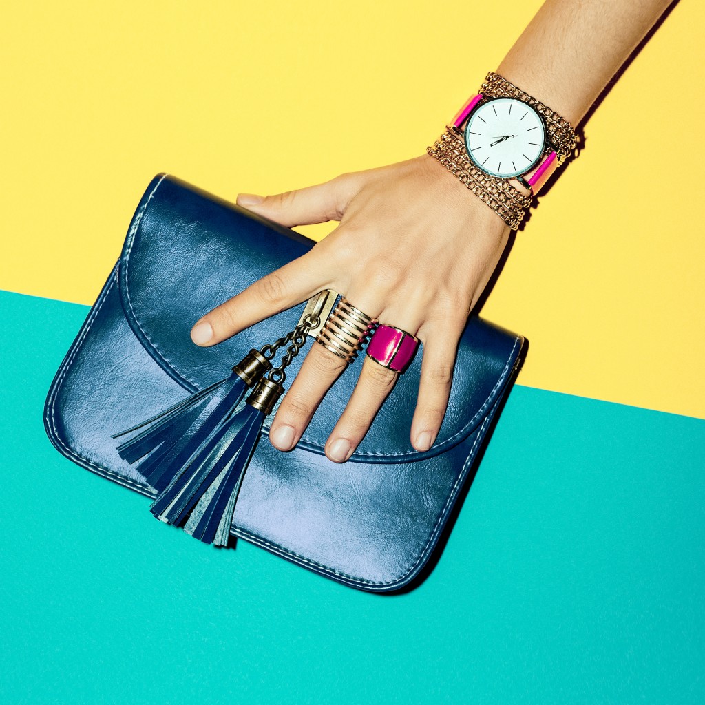 hand with bracelets, watch and rings holding a blue purse