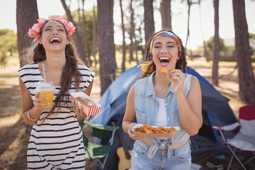 Happy friends eating snacks while camping in forest on sunny day