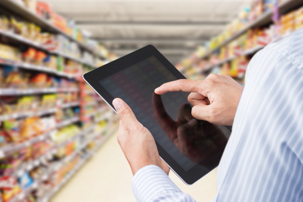 Businessman checking inventory in minimart on touchscreen tablet