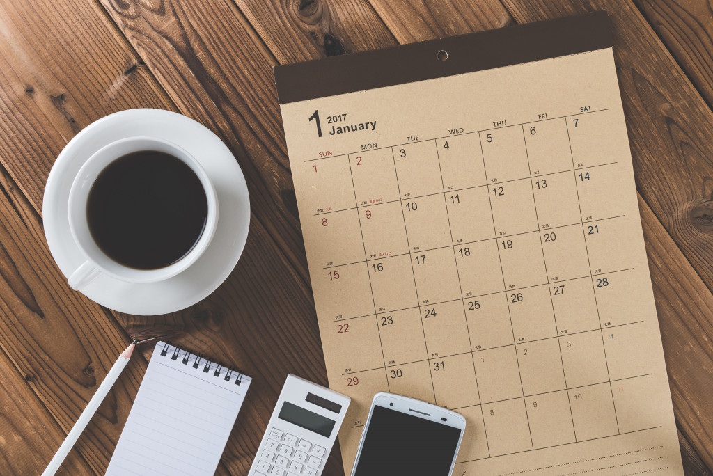 calendar, notepad, calculator, phone, and coffee cup on wooden background