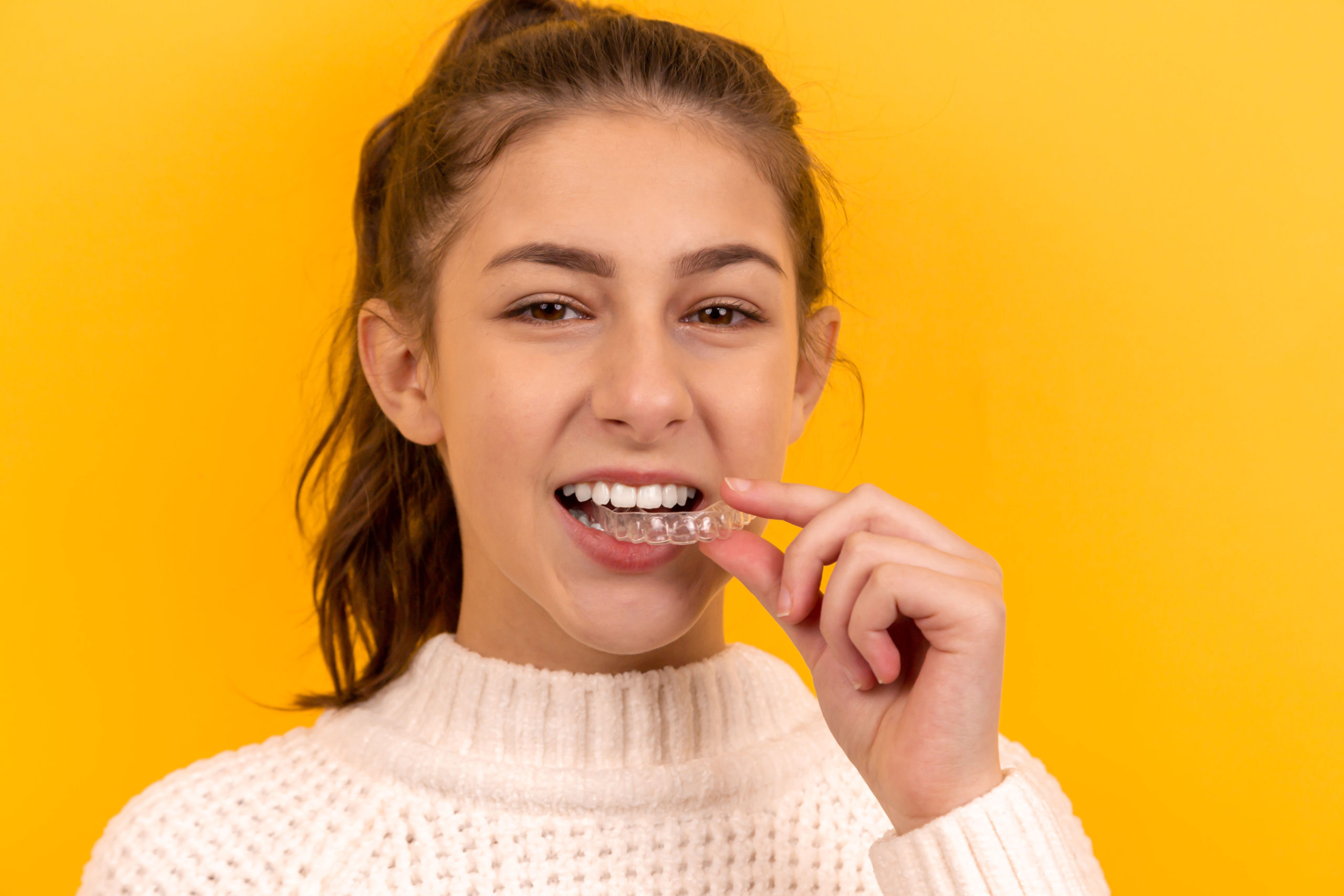 A beautiful girl puts a dental retainer on her teeth, she stands on a yellow background