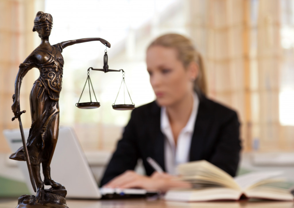female lawyer working in the background in her office with justice sculpture in foreground