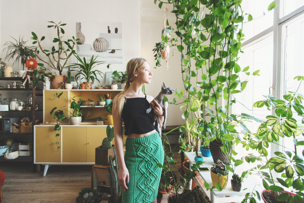 woman holding cat near window with vines and house plants all around