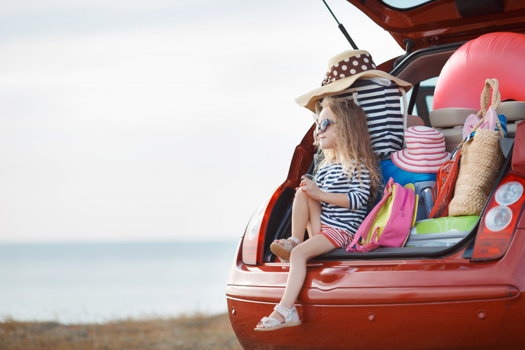 Little girl sitting at the back of a minivan filled with camping items.